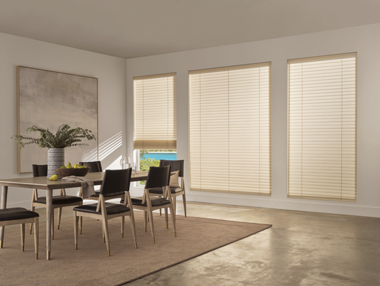 Three large windows in a modern dining room featuring Hunter Douglas Aria Fabric Blinds in a soft cream color, showing the subtle texture of the fabric slats against a neutral interior.