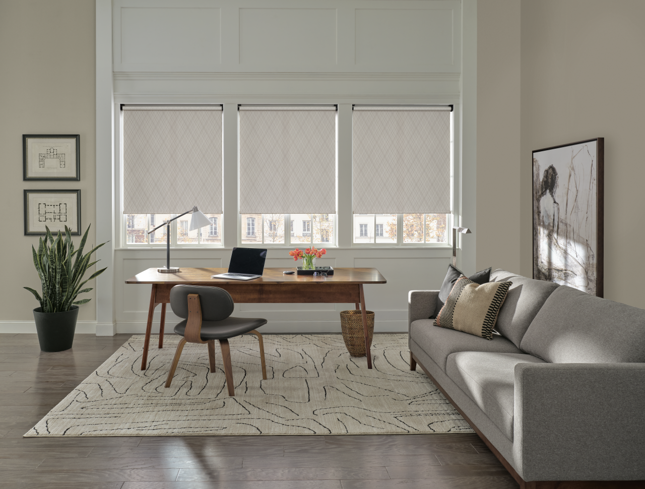 Hunter Douglas Designer Roller Shades in a modern home office featuring a wooden desk, grey sofa, and patterned area rug.